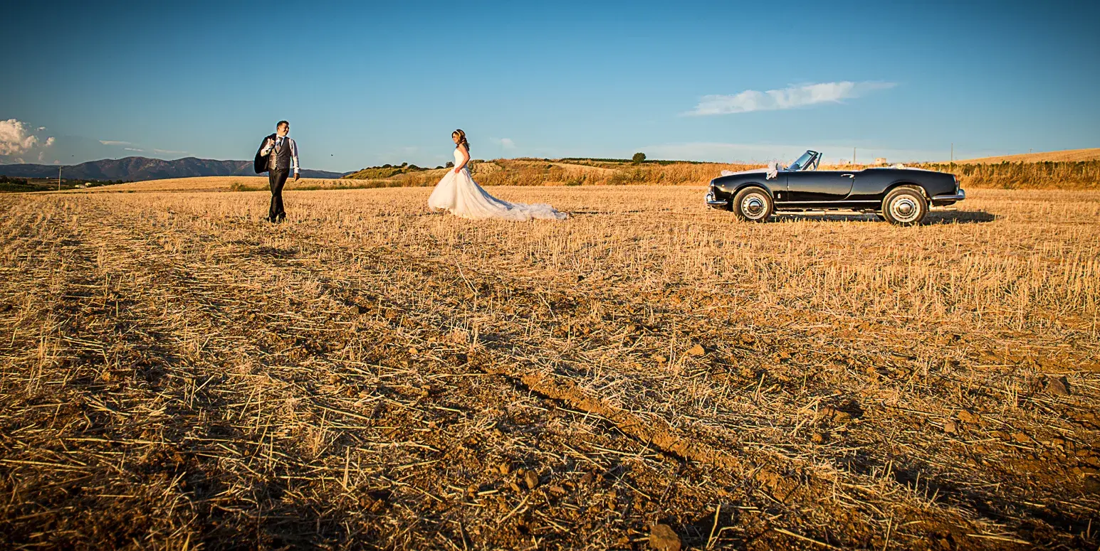 Sposi in un campo al tramonto con auto d’epoca